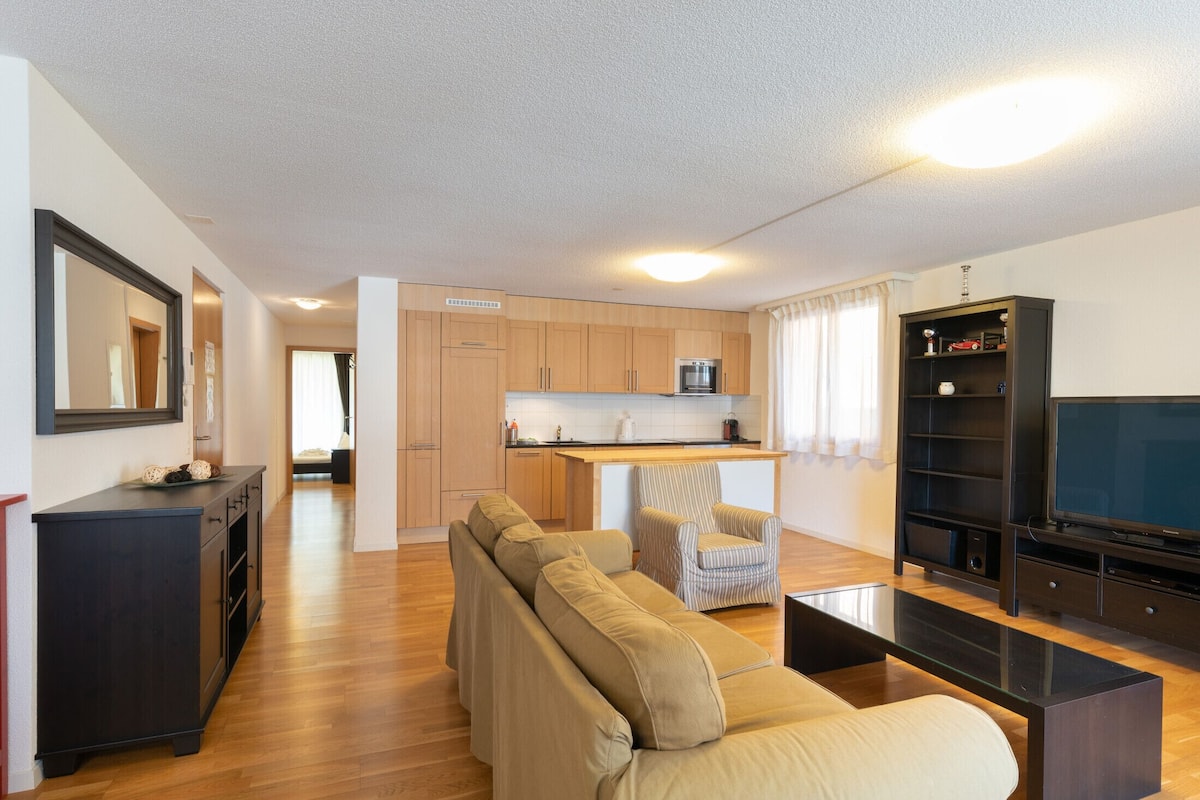 A modern living room with a sofa, a coffee table, a TV, and a kitchen area with wooden cabinets and a countertop.