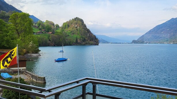 A balcony with a view of a lake, a flag, and a boat. - Chalet Apartments Iseltwald (Iseltwald)