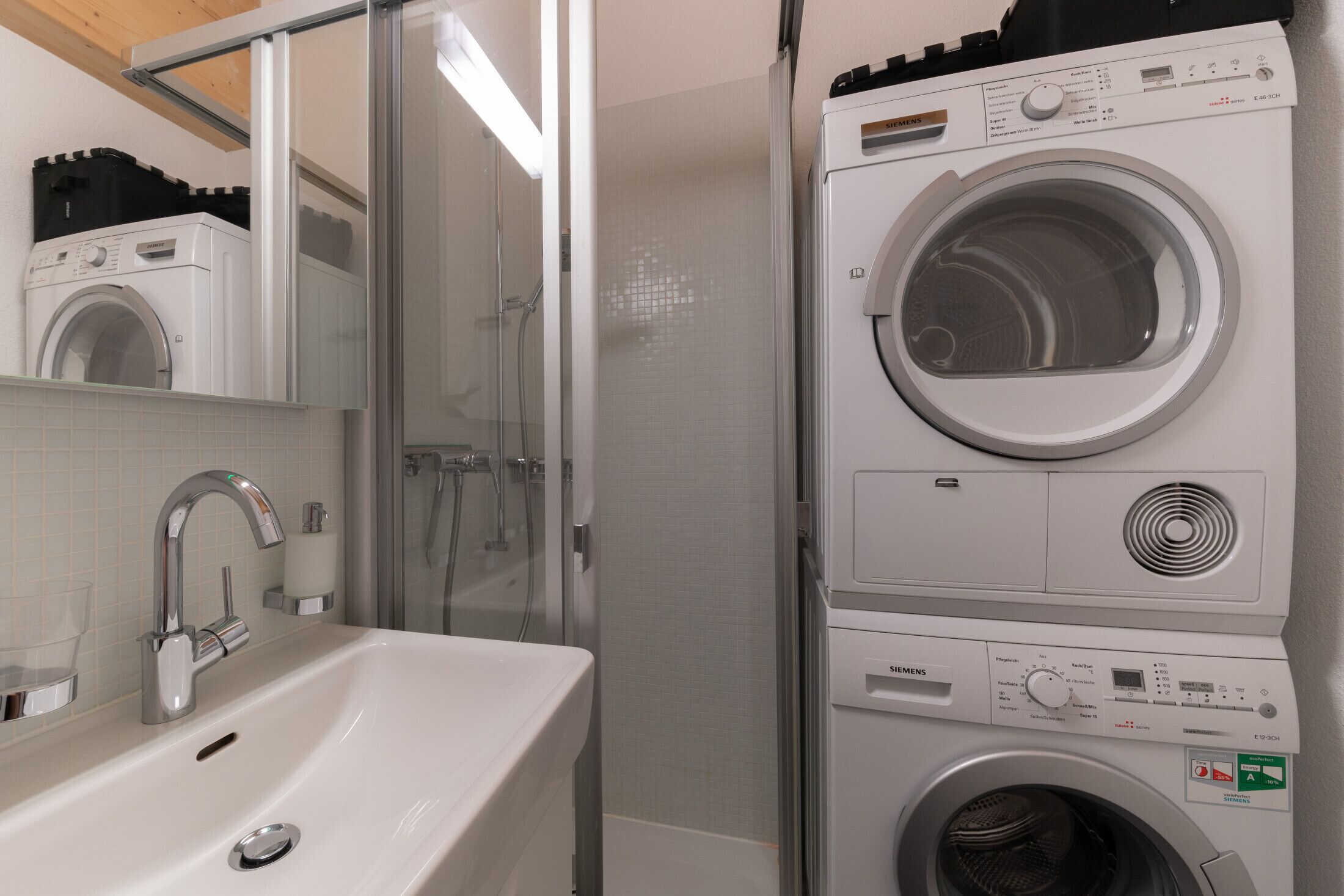 A compact laundry area with a washing machine and dryer, a sink with chrome fixtures, and a glass shower enclosure.