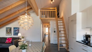 A modern kitchen with white cabinets, a wooden ladder, and a dining area with a table and chairs. - Chalet Apartments Iseltwald (Iseltwald)