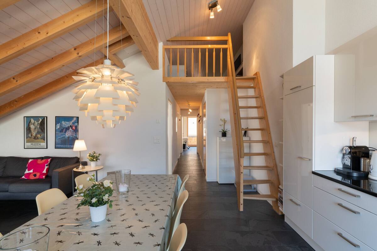 A modern kitchen with white cabinets, a wooden ladder, and a dining area with a table and chairs.