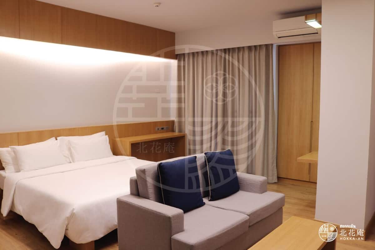 A hotel room with a bed, a sofa, a wooden headboard, a small table, and a curtain.