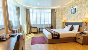 A hotel room with a bed, bedside table, lamp, and a desk with a chair. - Hotel Mirage Regency (Kathmandu)