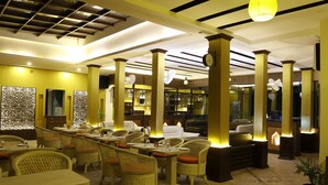 A restaurant with wicker furniture, a long communal table, and a modern ceiling design. - Hotel Mirage Regency (Kathmandu)