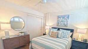 Une chambre à coucher comprenant un lit, des tables de chevet, une commode, un miroir et un ventilateur de plafond.