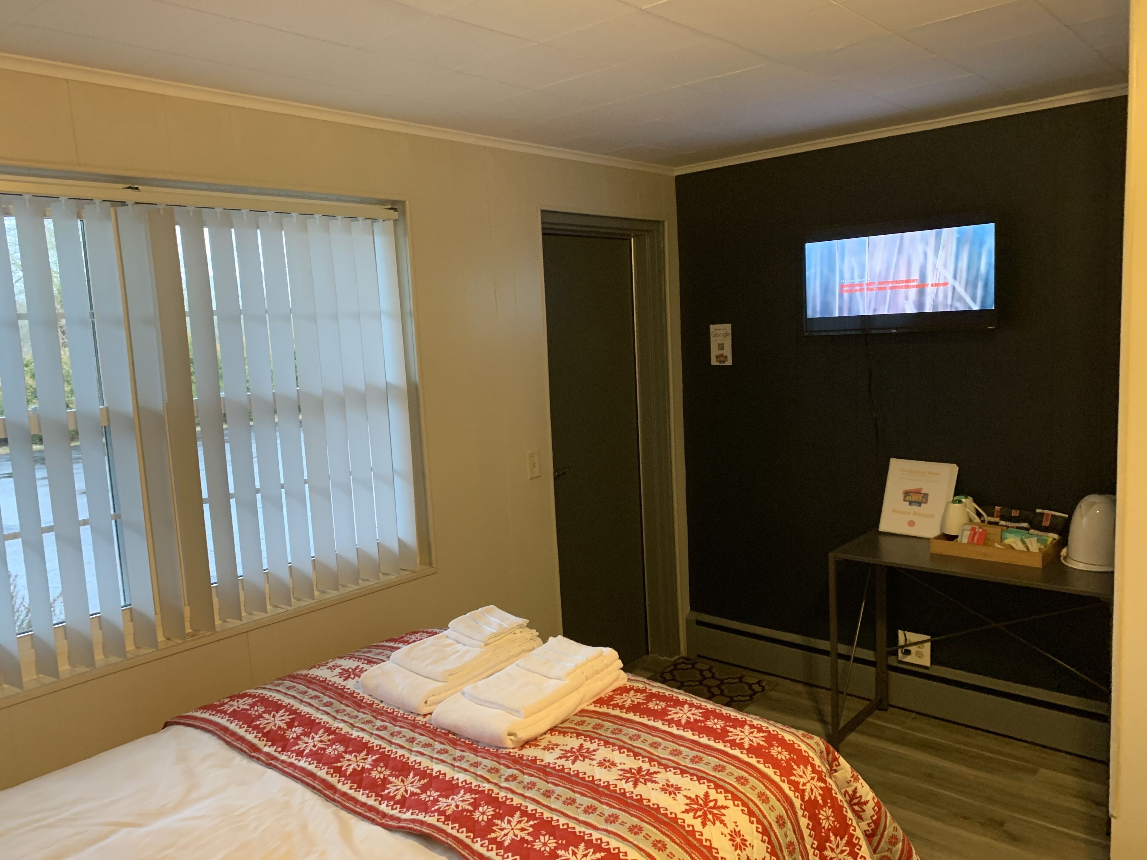 Une chambre d’hôtel avec un lit, un téléviseur fixé au mur et une petite table sur laquelle se trouvent un livre et une tasse.