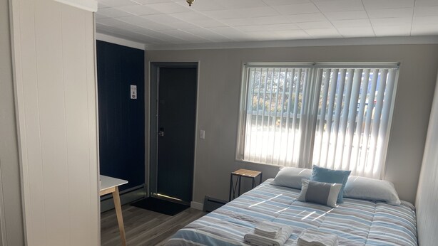 A bedroom with a bed, a desk, a door, and a window with blinds. - Yellow Springs Motel (Yellow Springs)