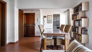 Un coin repas avec une table et des chaises en bois, une bibliothèque et, au fond, une cuisine.