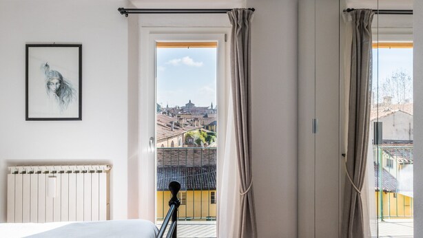 Une chambre avec un lit, un radiateur, une fenêtre avec des rideaux et une vue sur la ville.