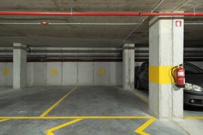 A parking garage with concrete pillars, yellow parking lines, and a fire extinguisher mounted on a pillar.