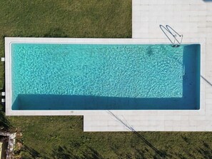 An aerial view of a rectangular swimming pool with clear blue water, surrounded by a white tiled deck.