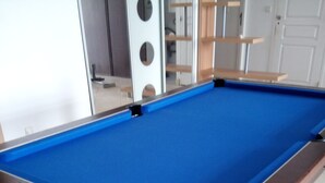 Ein Billardtisch mit blauem Filzbezug und Holzränder auf einem gefliesten Boden.