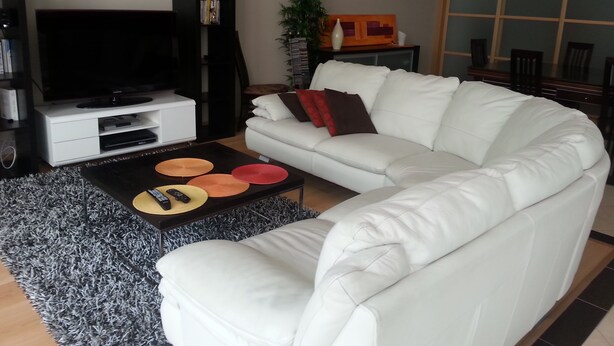 Ein modernes Wohnzimmer mit einem weißen Sofa, einem Flachbildfernseher, einem Couchtisch mit Fernbedienungen und einem Bücherregal.