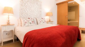 A neatly arranged bedroom with a bed, two bedside tables with lamps, a decorative wall panel, and a wooden door leading to a bathroom.