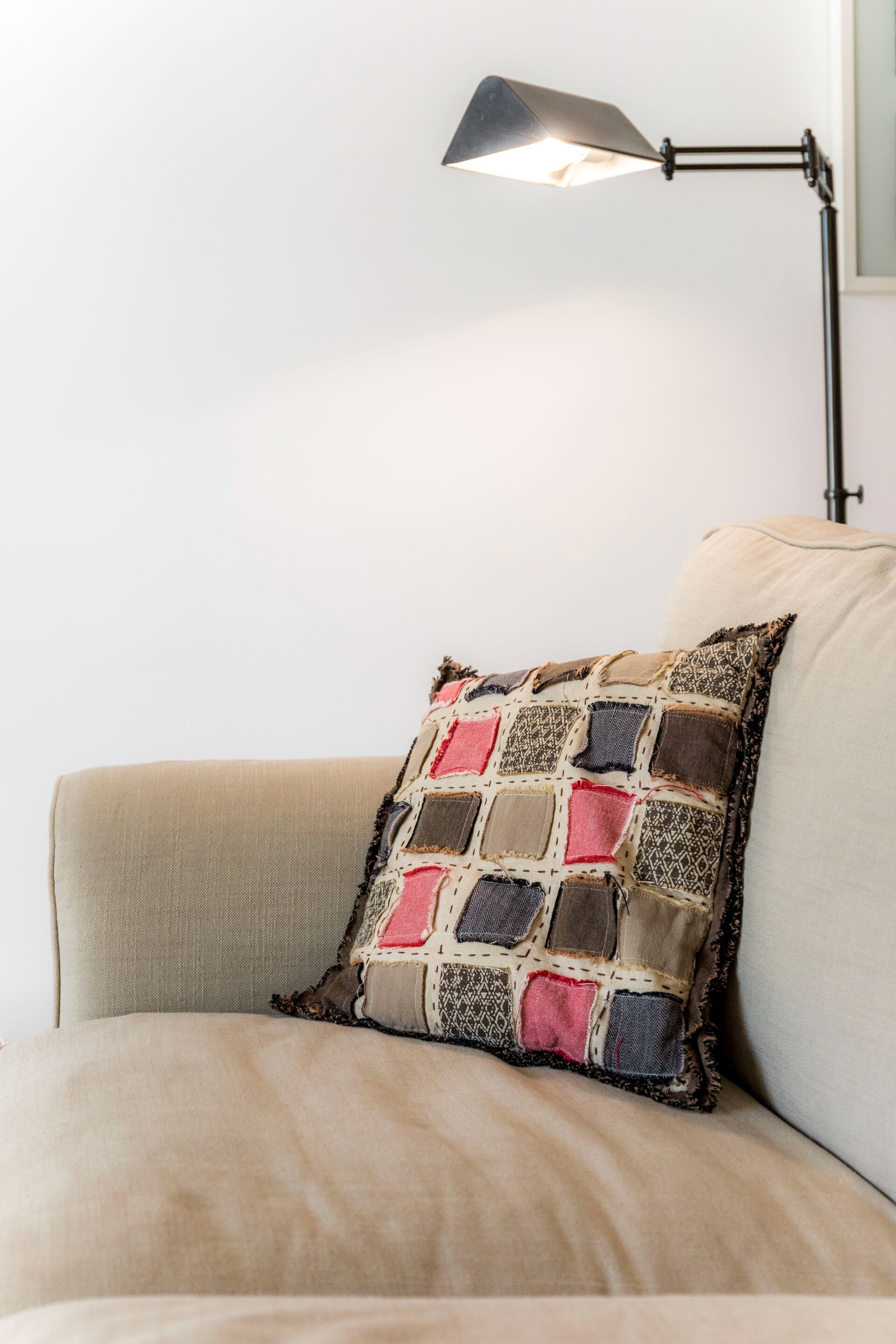 Un sofá color beige con un cojín de patchwork y una lámpara de pie negra.