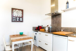 Una cocina compacta con una mesa de madera, sillas blancas, lavadora y lavavajillas integrado.