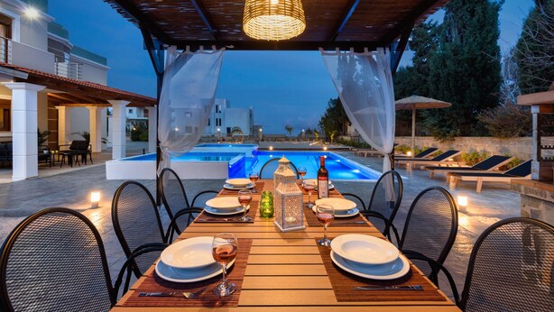 An outdoor dining area with a pool view, tables set with plates and glasses, and a decorative lantern. - Aileen Villa with Private Pool (Κοσκινού)