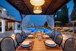 Ein Essbereich im Freien mit Blick auf den Pool, Tische sind gedeckt mit Tellern und Gläsern, und ein dekorativer Laterne.