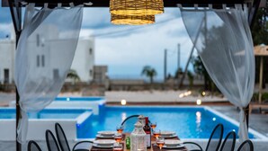 An outdoor dining area with a pool view, featuring a table set for four with chairs, a lantern, and a bottle of wine. - Aileen Villa with Private Pool (Κοσκινού)
