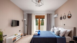A bedroom with a bed, a TV, a bedside table, a lamp, and a window with curtains. - Aileen Villa with Private Pool (Κοσκινού)