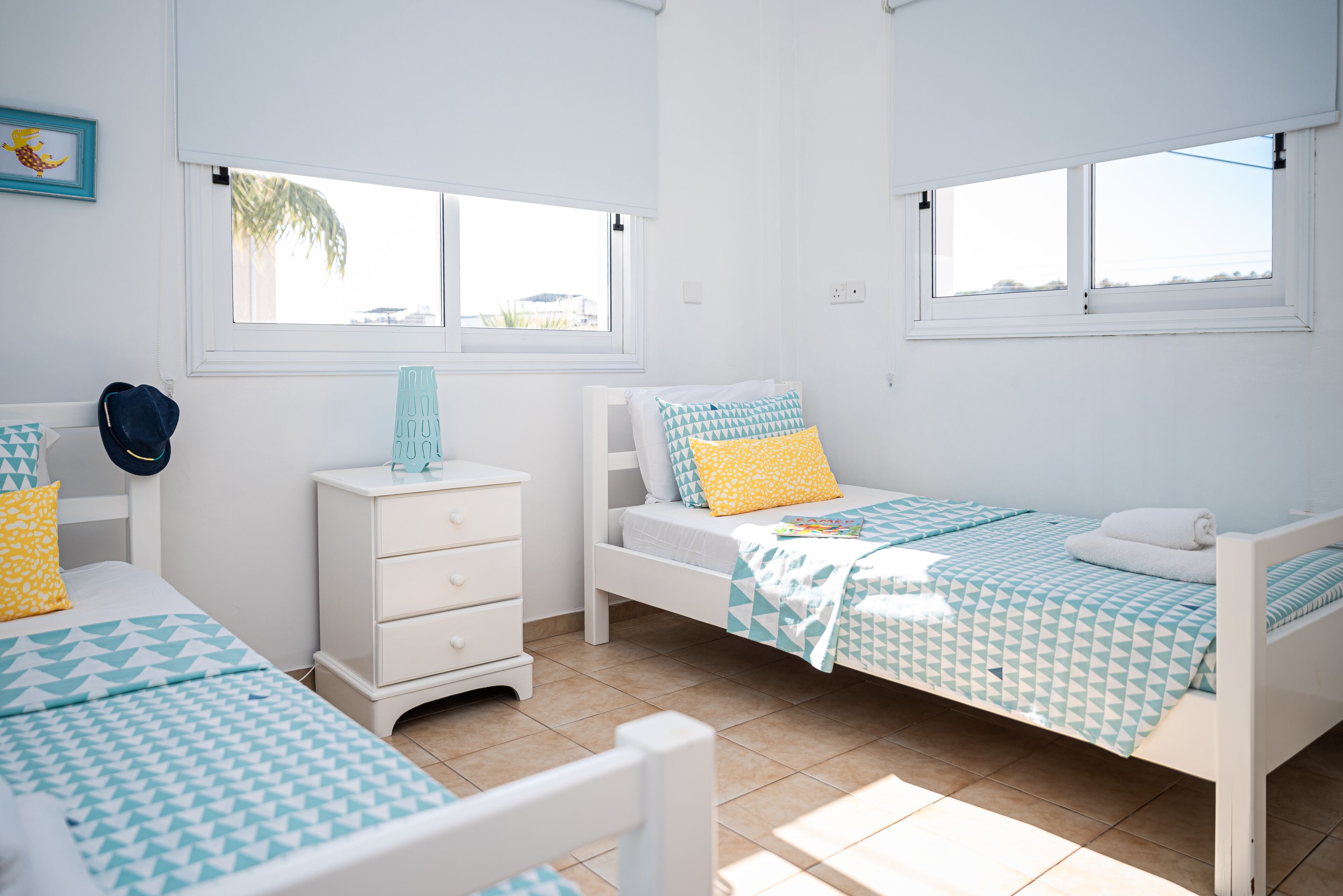 A bedroom with two beds, a dresser, and two windows.