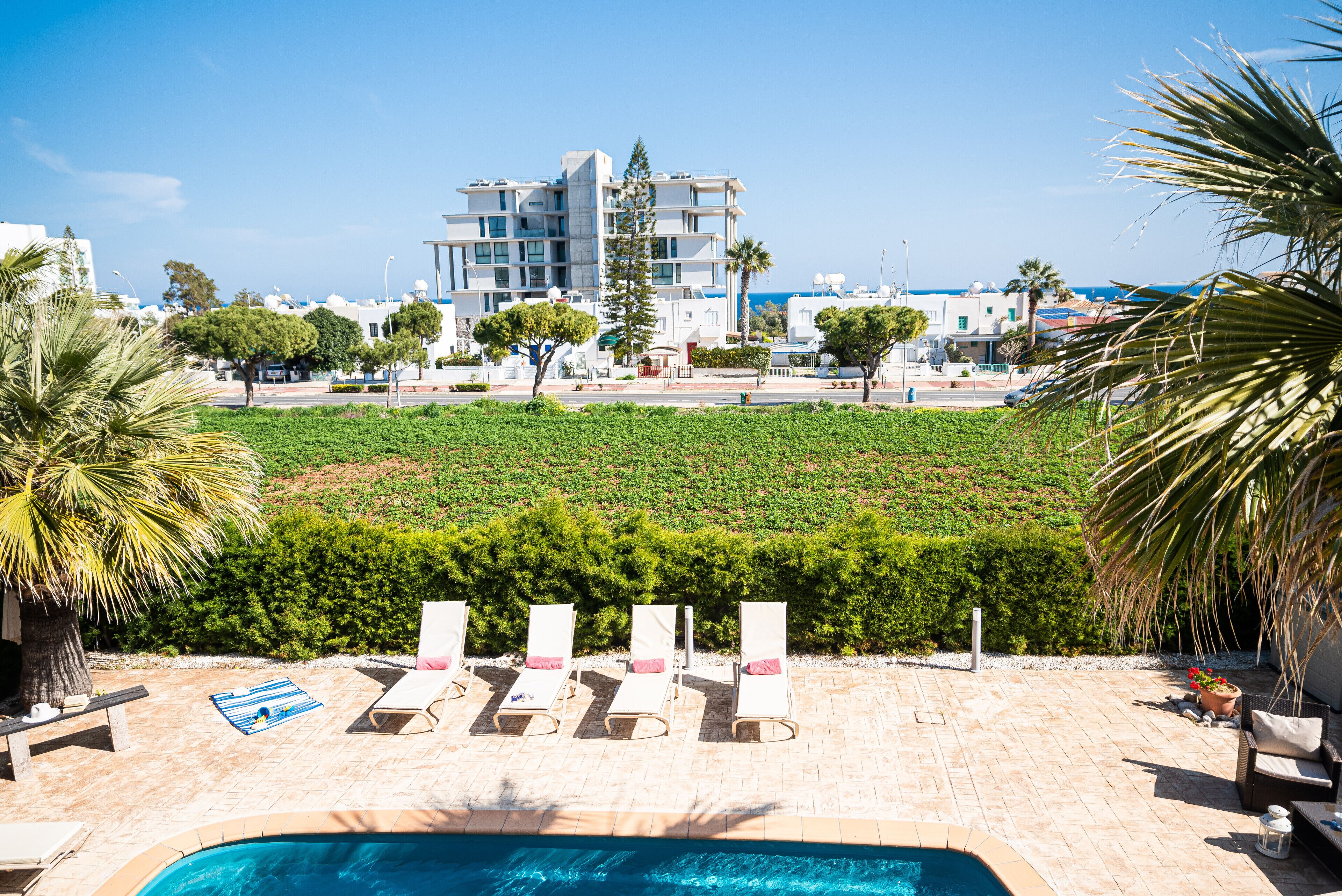 A pool area with lounge chairs, a small pool, and a view of buildings and greenery.