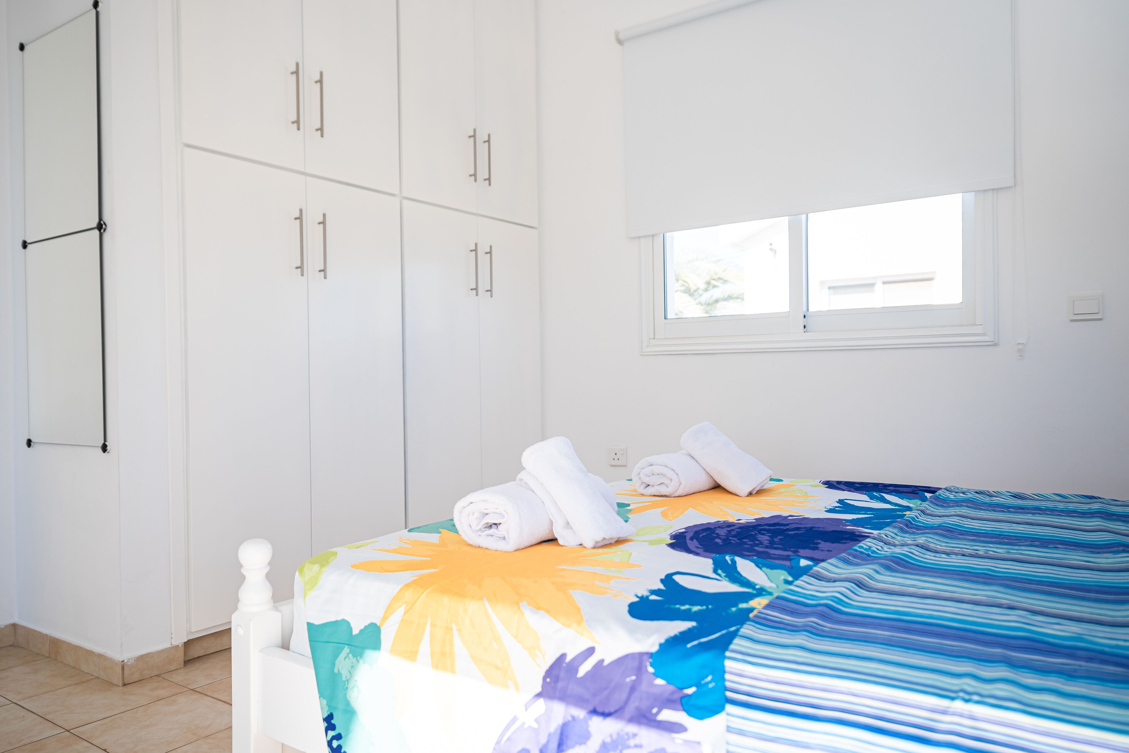 Quarto com cama, guarda-roupa branco e janela.