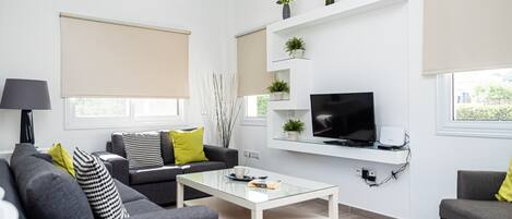 A modern living room with a sofa, coffee table, TV, and shelves with plants.