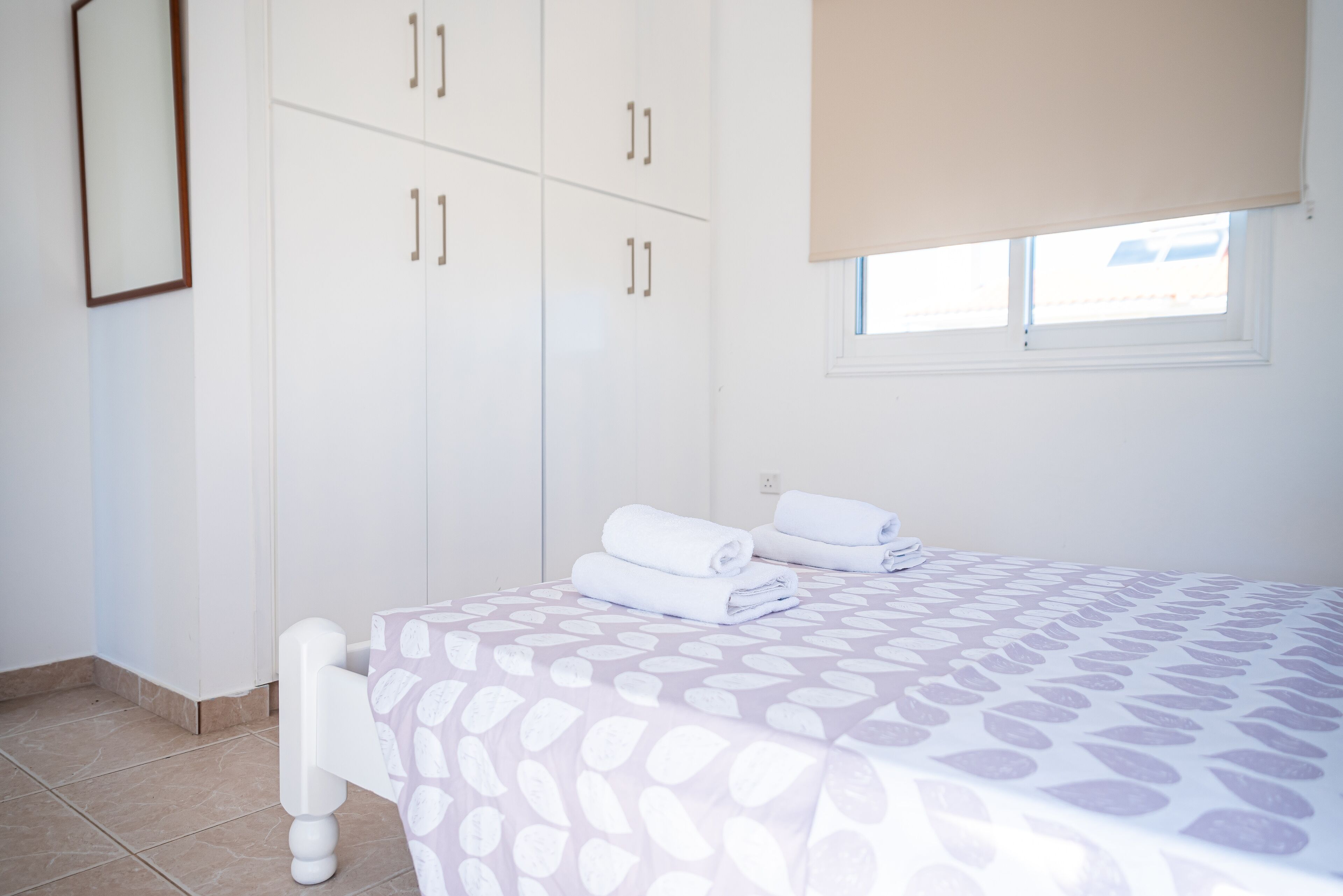 A bedroom with a bed, white wardrobe, and a window with a blind.