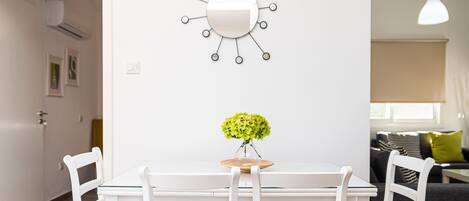 A dining area with a white table and chairs, a vase with yellow flowers, and a wall-mounted mirror.