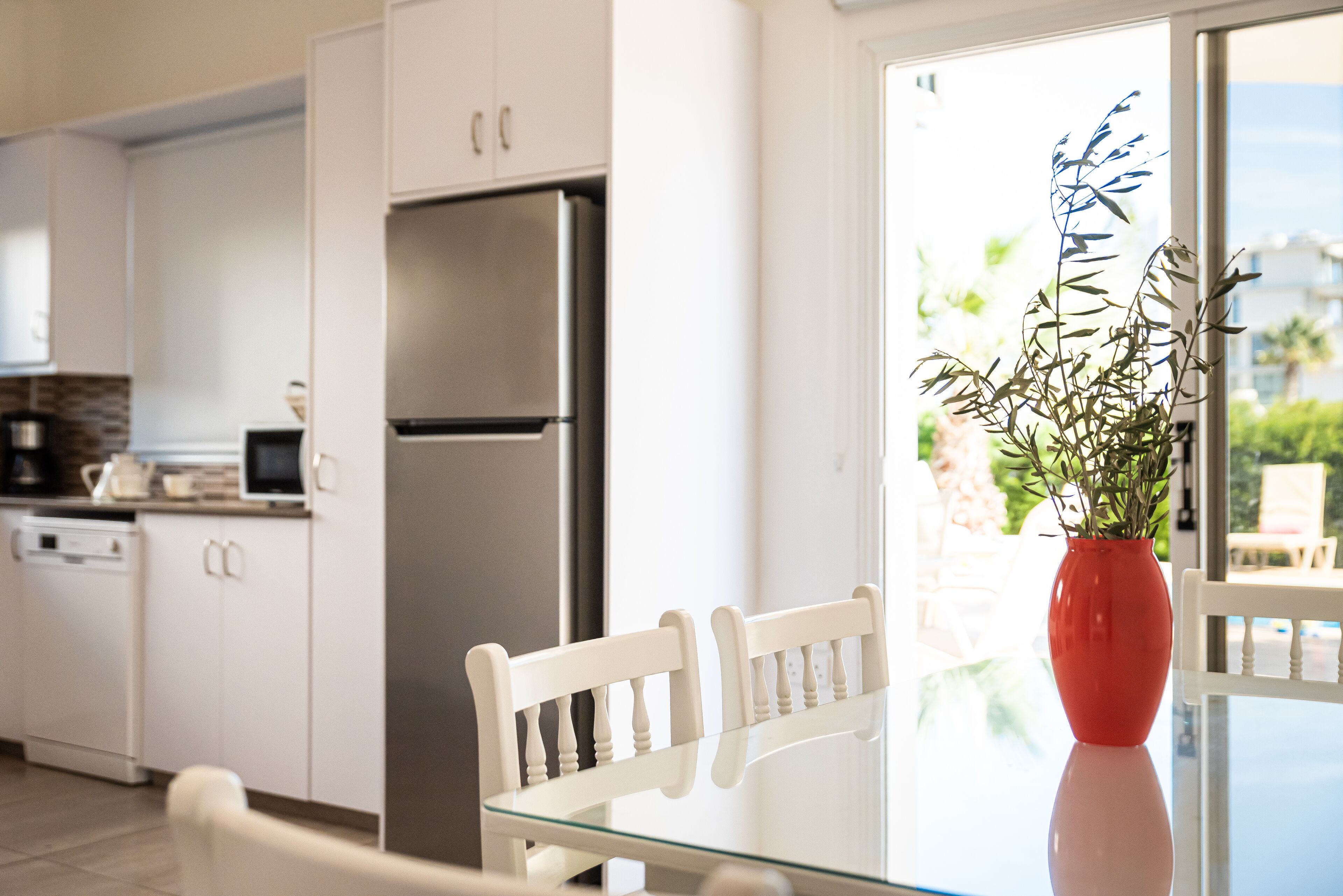 A modern kitchen with white cabinets, a stainless steel refrigerator, and a glass dining table.