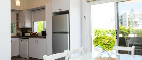 A modern kitchen with white cabinets, a stainless steel refrigerator, and a dining area with a glass table and white chairs.