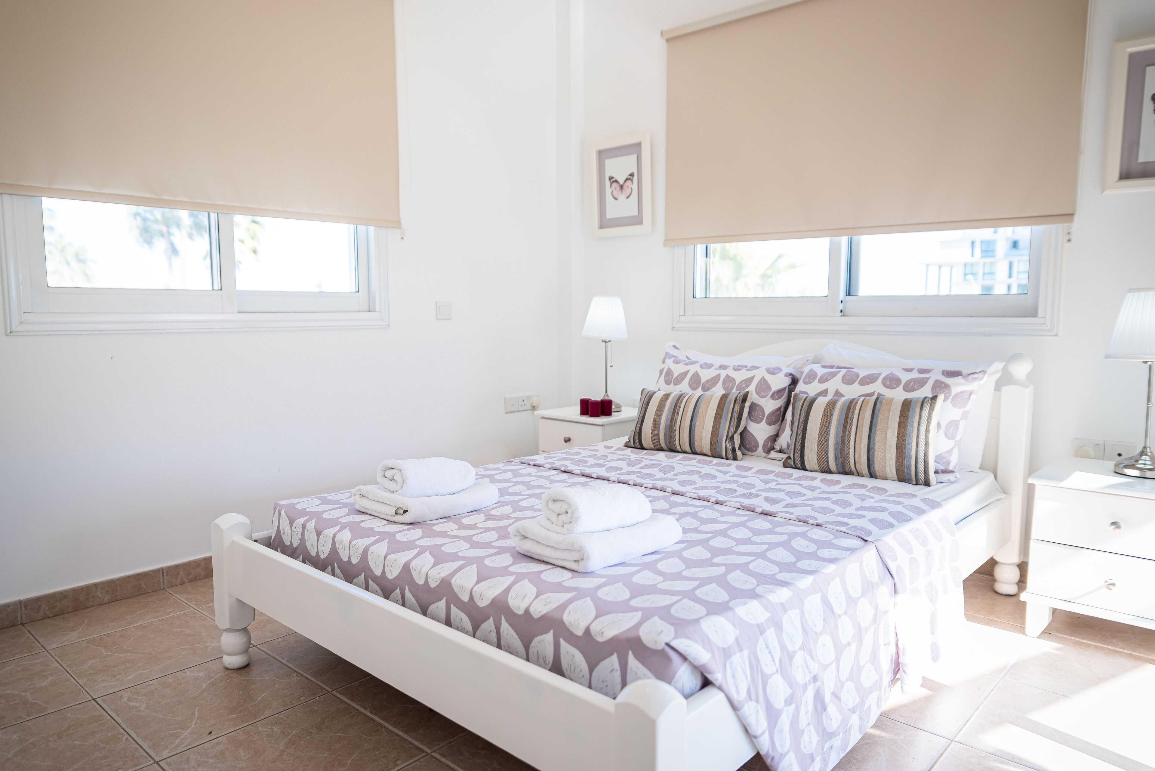 A bedroom with a bed, two bedside tables, a nightstand, a lamp, and a window with a view.