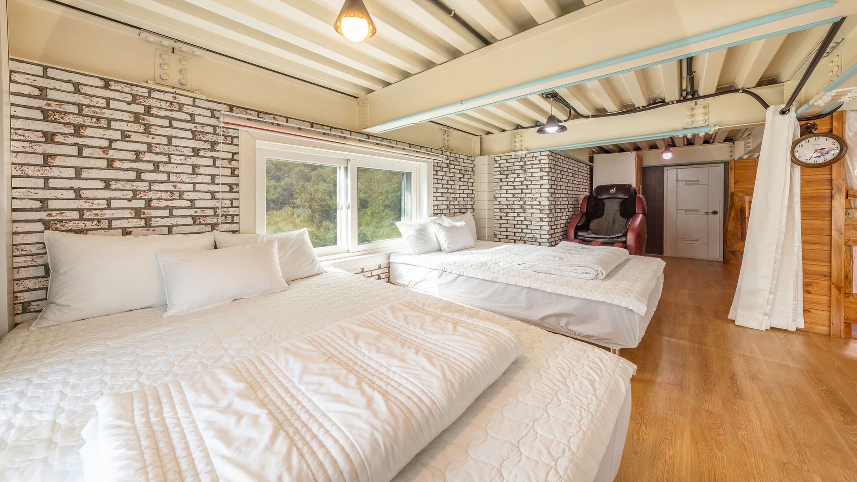 Une chambre avec deux lits, un mur en briques, une fenêtre et un fauteuil de massage.