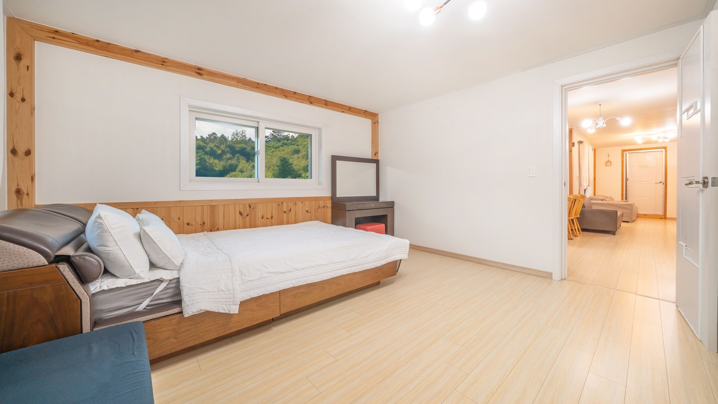 A bedroom with a bed, a TV, a window with a view of trees, and a wooden floor.