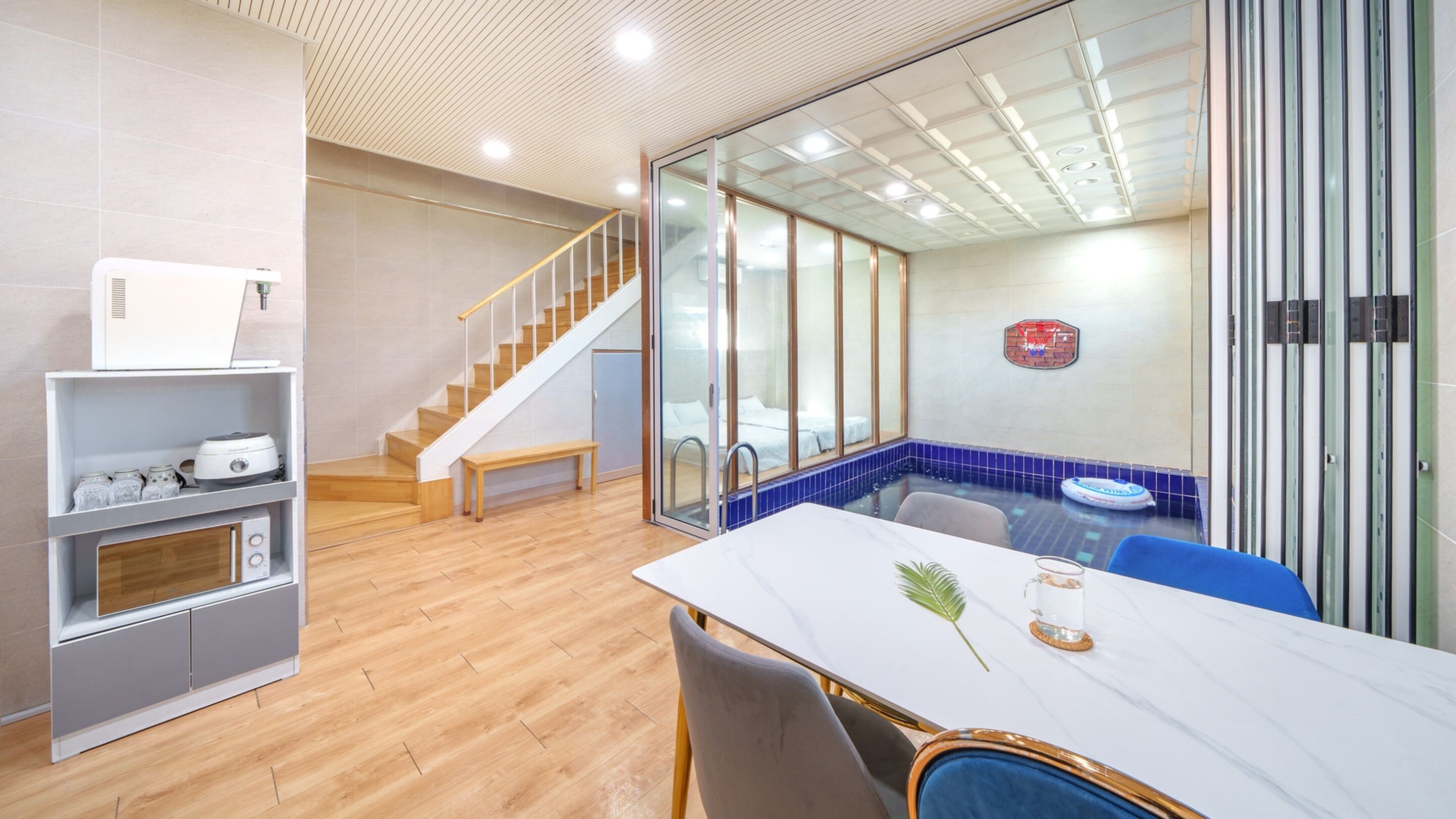 Une cuisine moderne dotée d’une cuisinière intégrée, d’un escalier en bois, d’une salle de bain fermée par des parois de verre et d’un coin repas avec une table en marbre.