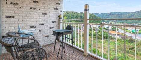 Un balcón con sillas de mimbre, una mesita y vistas a un paisaje verde con colinas.