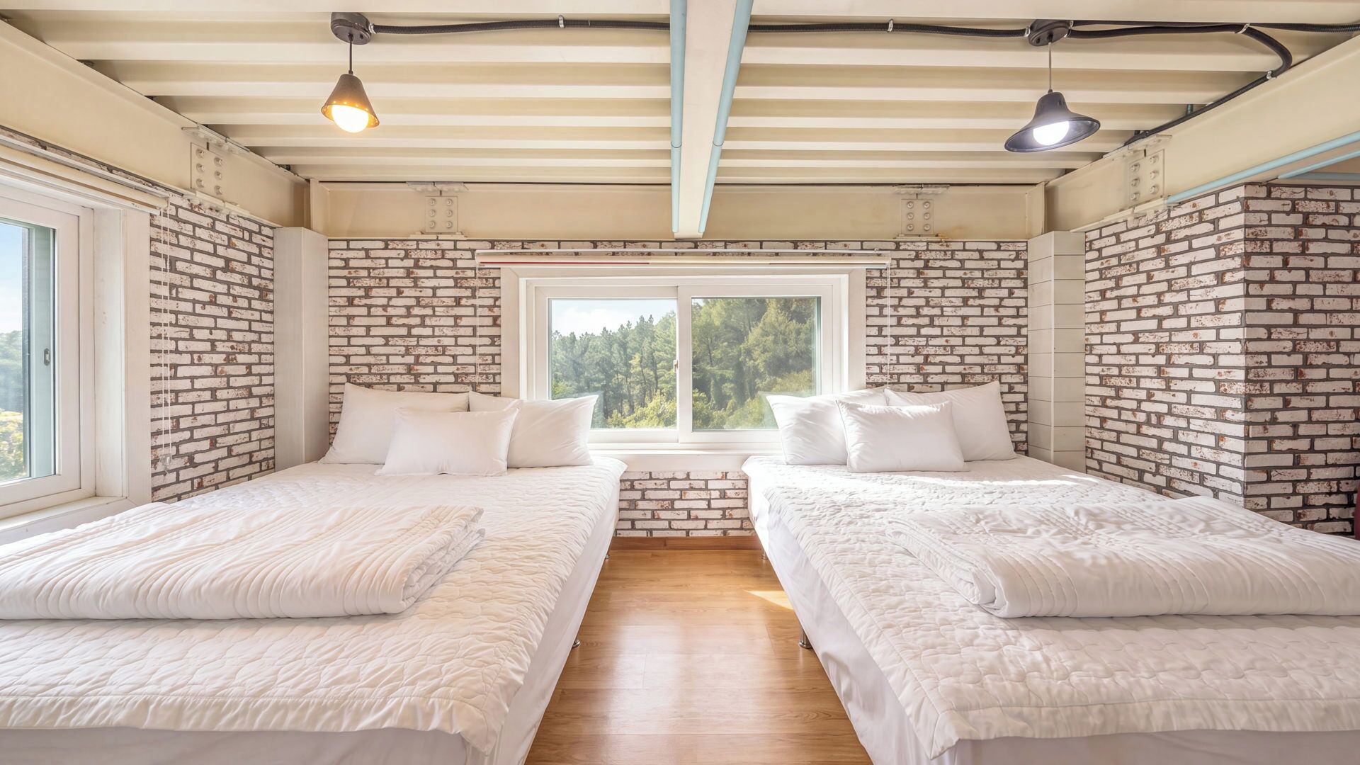 Una habitación con dos camas, una ventana, paredes de ladrillo y piso de madera.