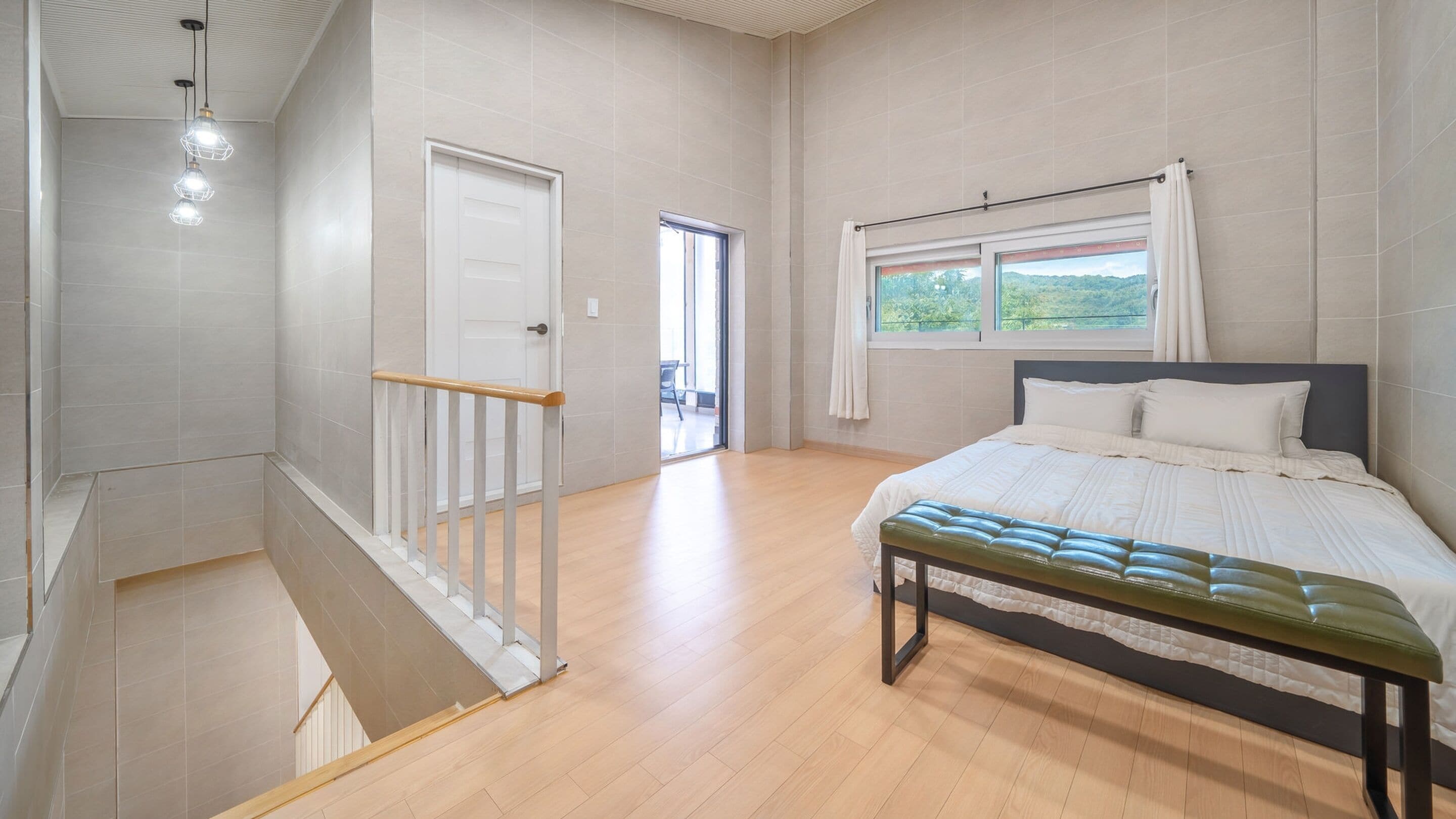 A bedroom with a bed, a bench, a window with a view, and a door leading to another room.