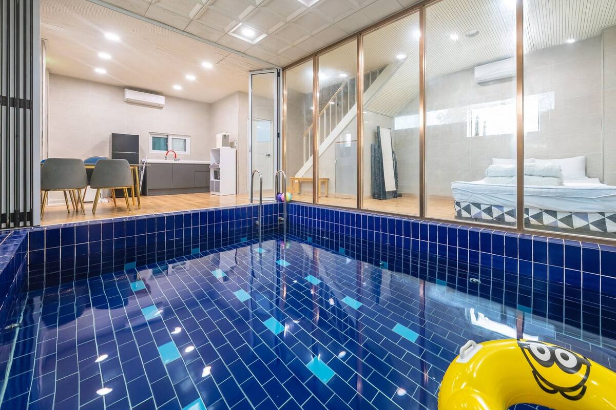 A modern hotel room with a large pool, a bed, and a kitchenette.