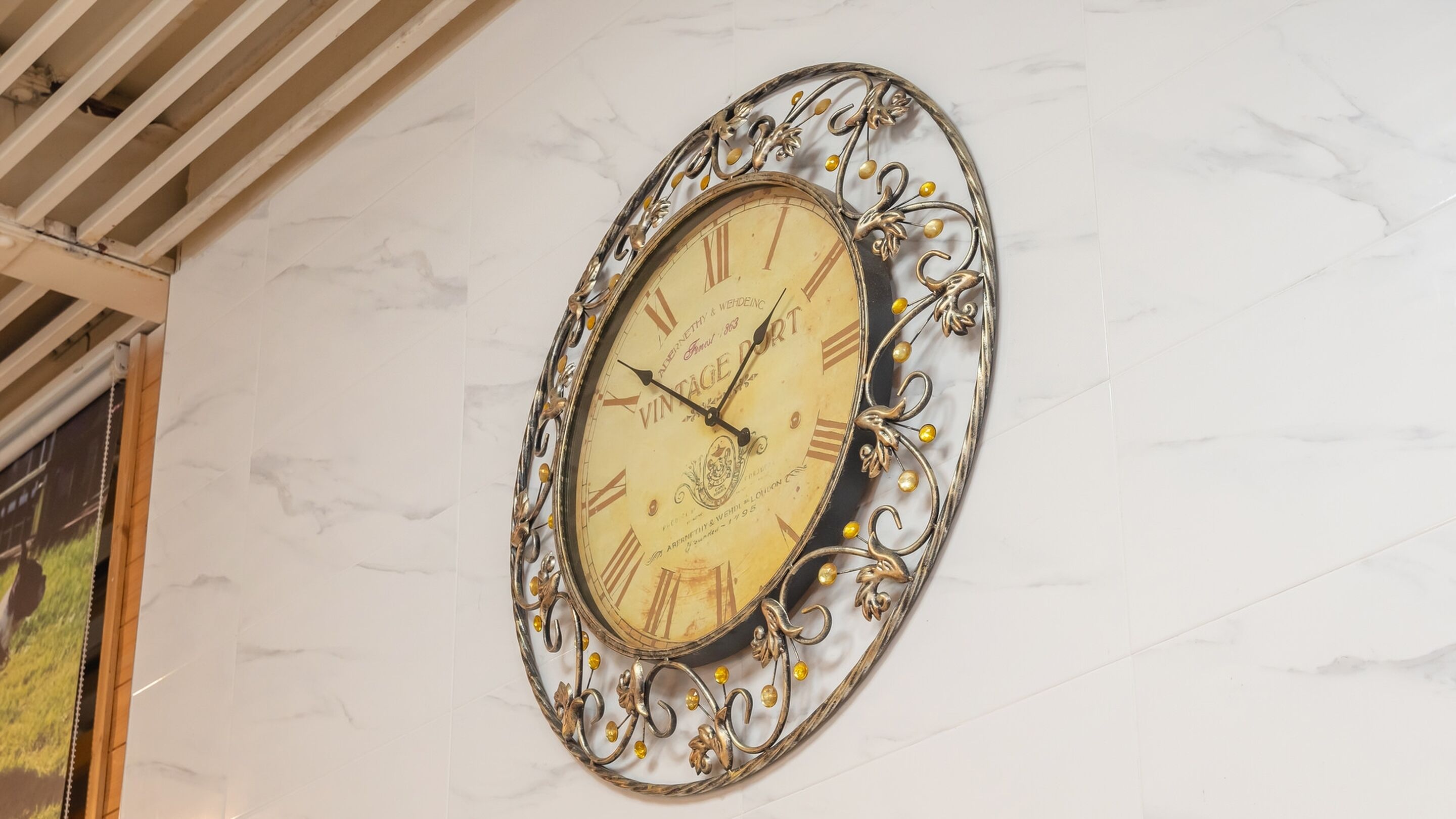 A wall-mounted vintage-style clock with ornate metalwork and yellow accents.