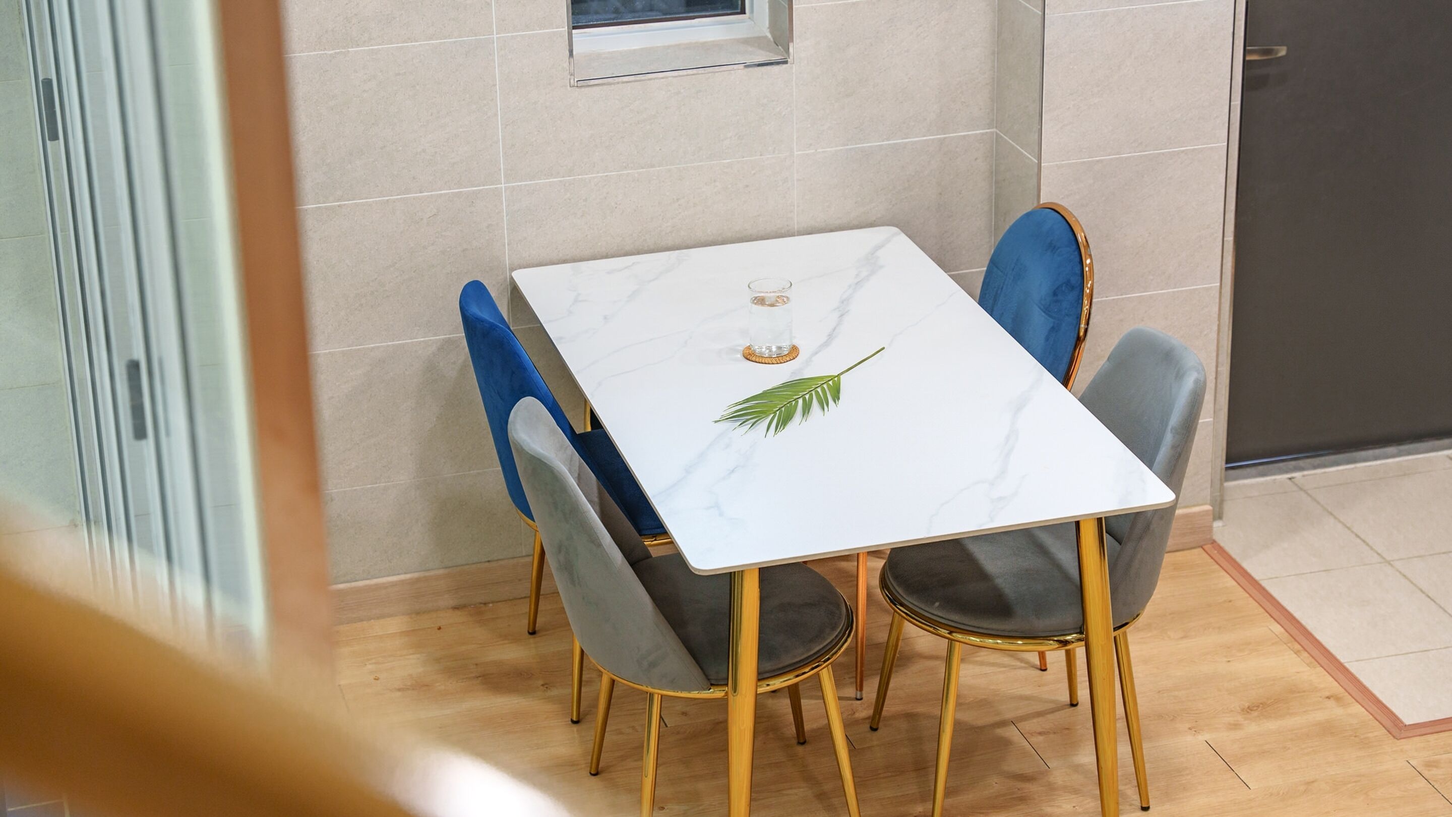 Un comedor con una mesa de mármol blanco, dos sillas azules y una silla dorada.