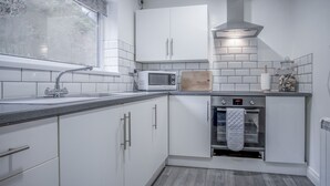 Uma cozinha moderna com armários brancos, micro-ondas, forno e janela com vista para árvores.