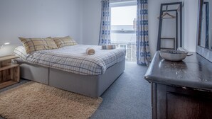 Quarto com cama, mesa de cabeceira e janela com cortinas.