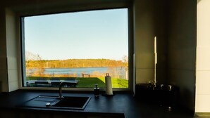 Et moderne køkken med et stort vindue der ud til sø og skov.