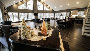 Un salón amplio con un piano, una chimenea y un gran ventanal con vistas a un paisaje nevado.