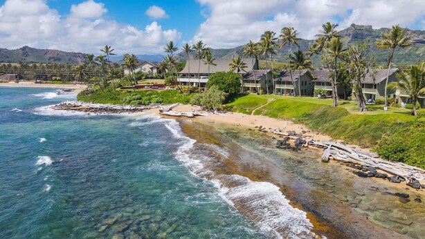 Ein Strandhotel mit klarem Meerblick, einem Sandstrand und üppiger Vegetation.