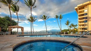 A pool area with lounge chairs, palm trees, and a building in the background. - Oceanfront Wailea condo w/ Molokini views and pool access (Wailea)