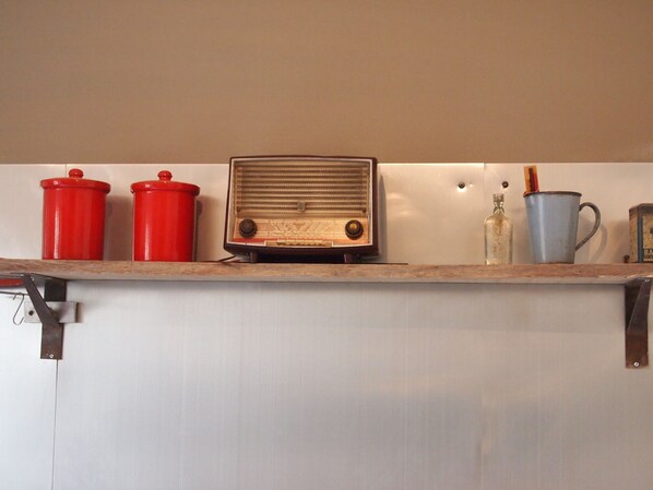 A kitchen counter with a vintage radio, red containers, a blue mug, and a bottle.