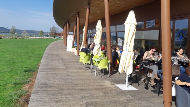 Un espace extérieur aménagé avec des tables et des chaises, situé sous un toit abrité et offrant une vue sur un champ verdoyant.